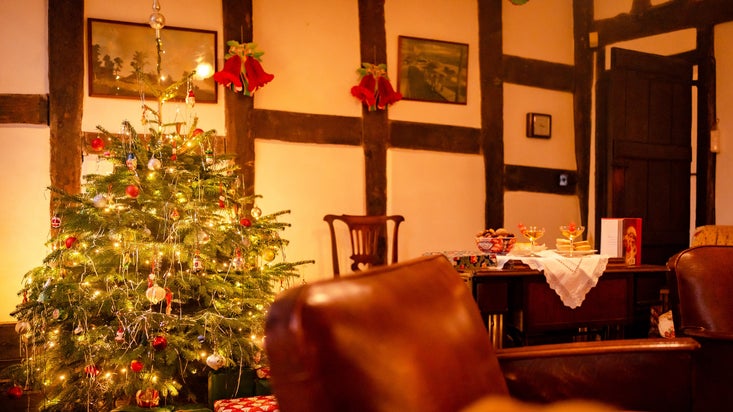 A tinsel and fairy-light decorated Christmas tree in the corner of a room, next to a table filled with sweets and baby Cham glasses.